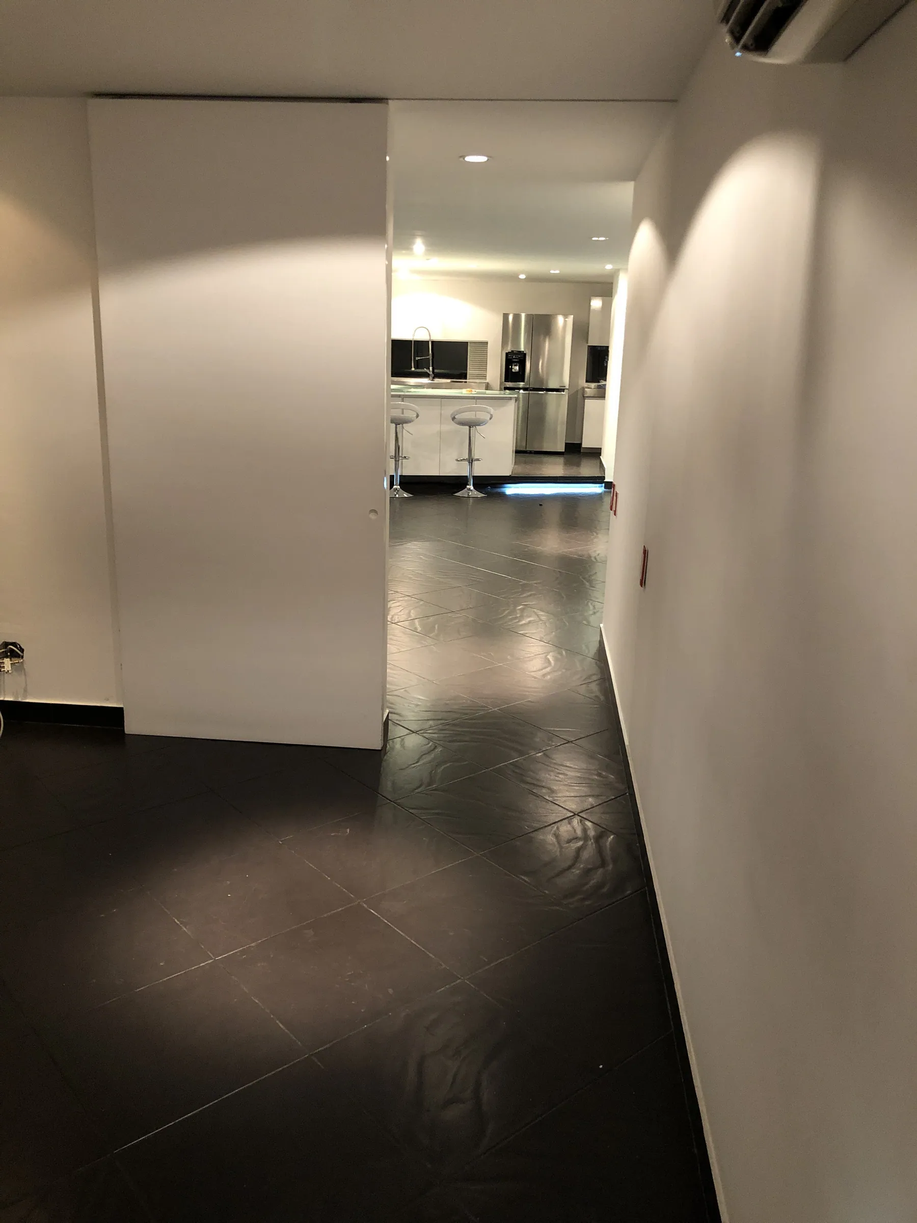 Hallway in dark stone leading past a sliding door into the lit kitchen