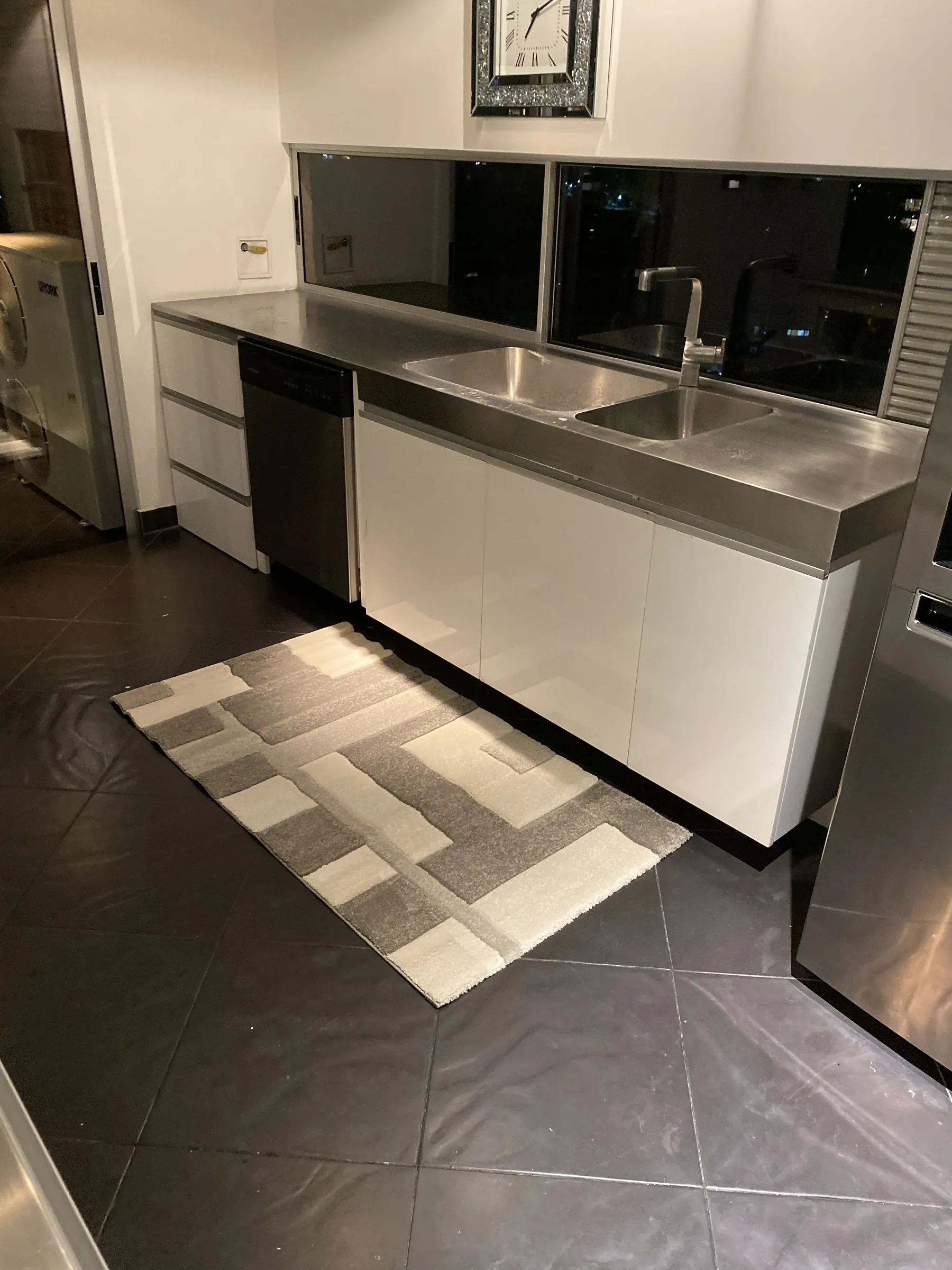 Stainless steel prep run with double sink and integrated dishwasher, dark glass backsplash and the city beyond