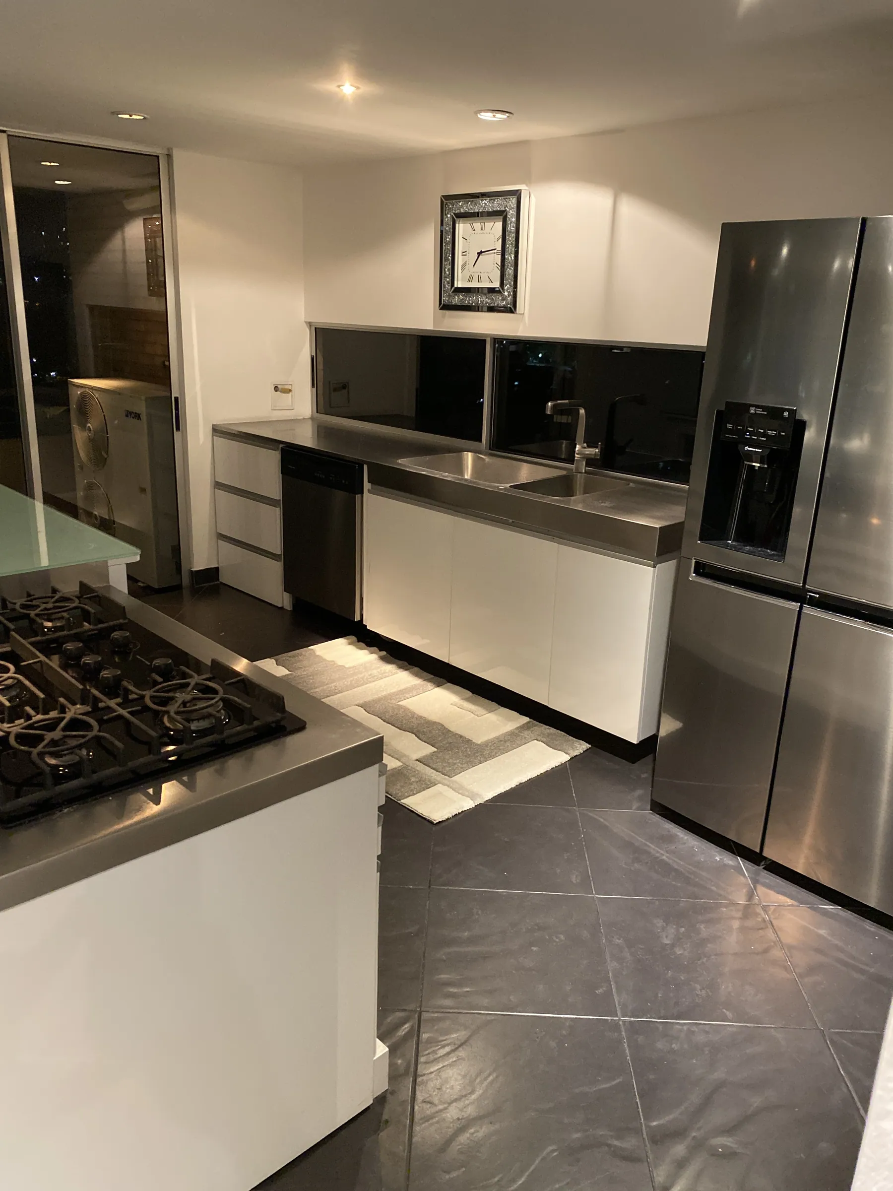 Stainless prep counter and double sink beside a full-height French-door refrigerator, with the laundry beyond
