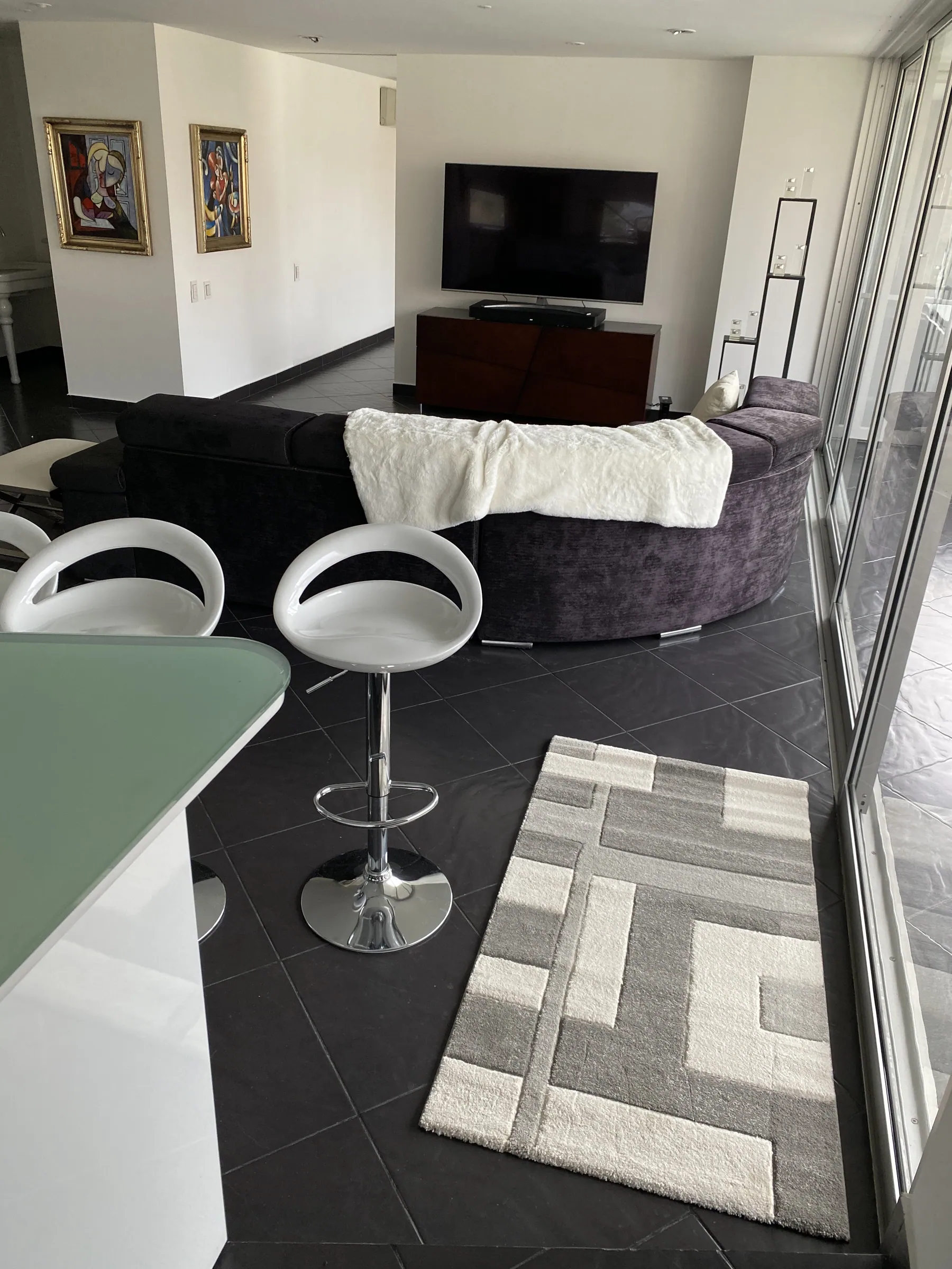 Lounge area with framed artwork, wall-mounted television, curved sectional and a geometric wool rug on dark stone floors