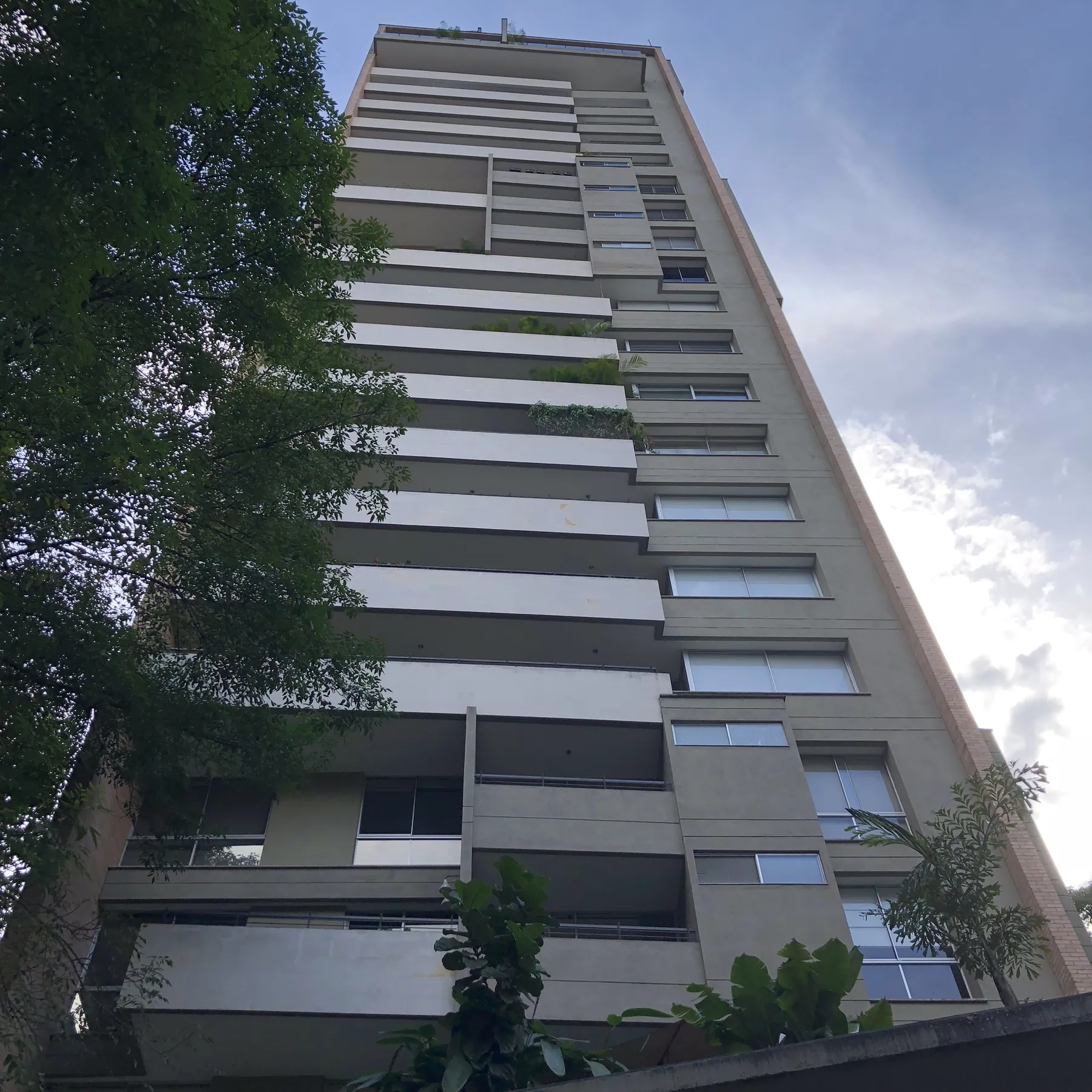 Exterior of Edificio Hills, a tower with vertical concrete fins and cantilevered volumes set against greenery