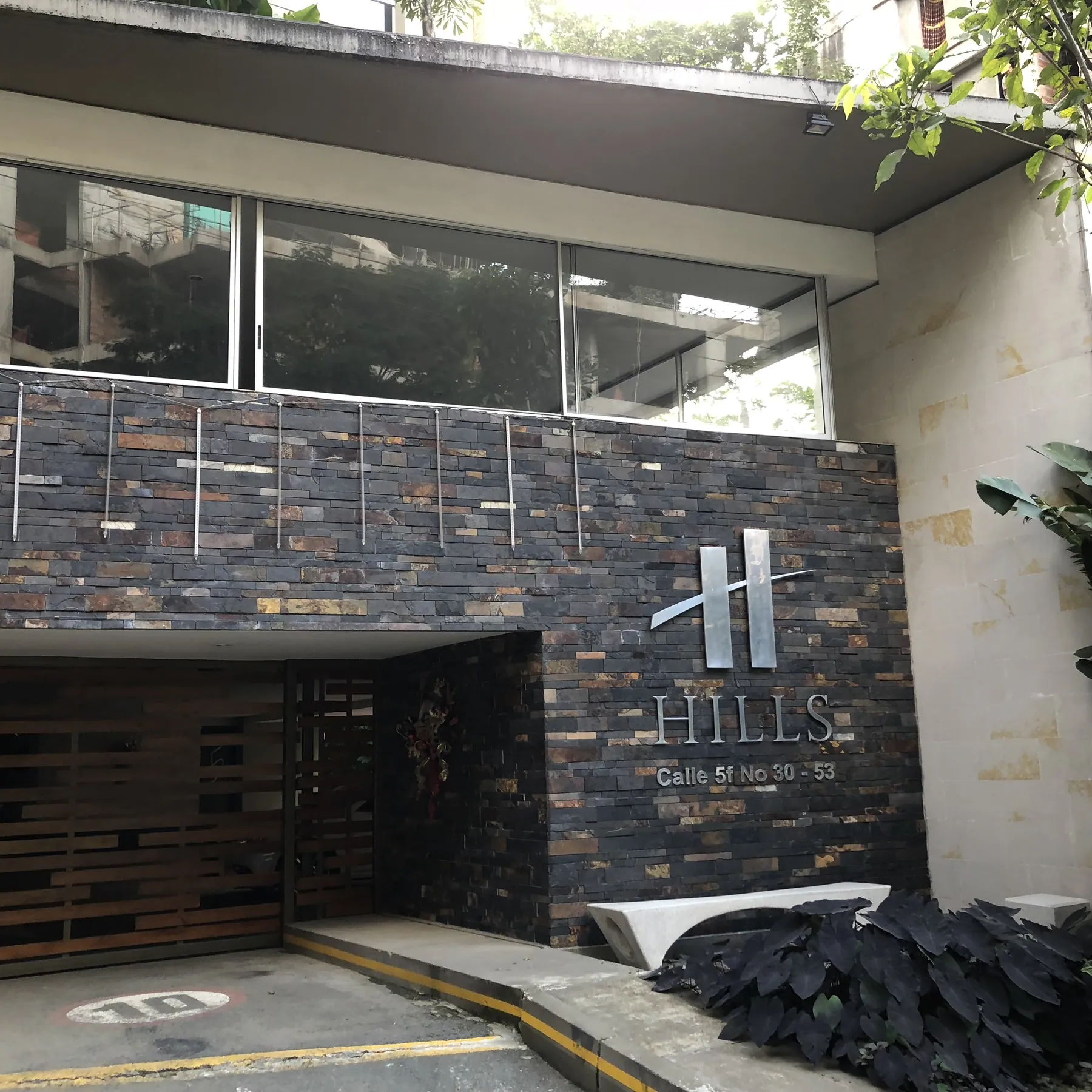 Building entrance with a stacked slate wall, brushed steel HILLS lettering and the street number Calle 5F No 30-53