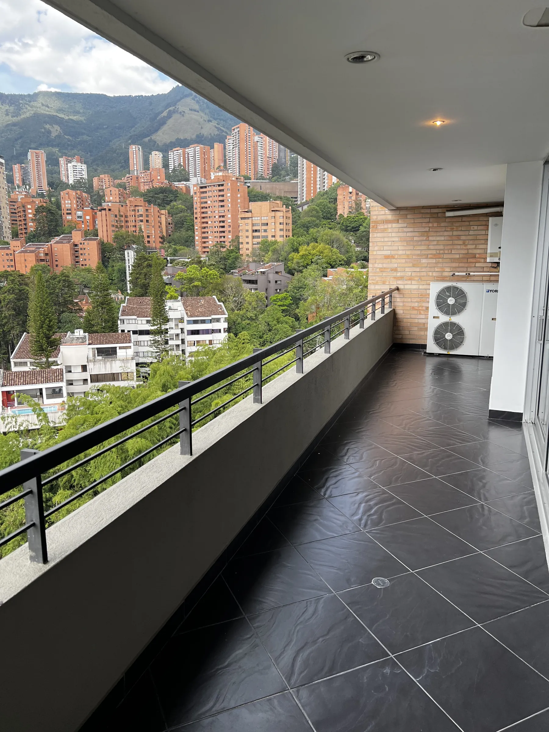 The terrace running the length of the glazed façade, hillside and Los Balsos towers beyond the railing