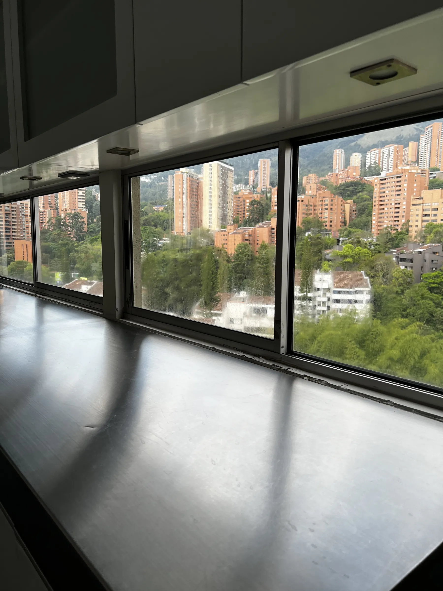 Stainless counter running the length of the window line, city and green hillside beyond the glass